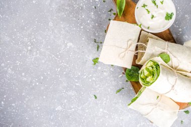 Vejetaryen taze tortilla sebzeyle sarılır. Taze pita ruloları, tofu, salatalık, bebek ıspanağı ve avokado. Gri beton arka plan kopyalama alanı