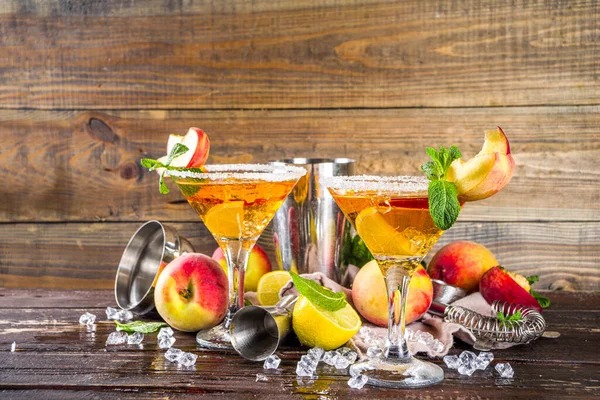 Refreshing summer drink, peach martini cocktails with gin or vodka and fresh peach garnish, wooden background copy space