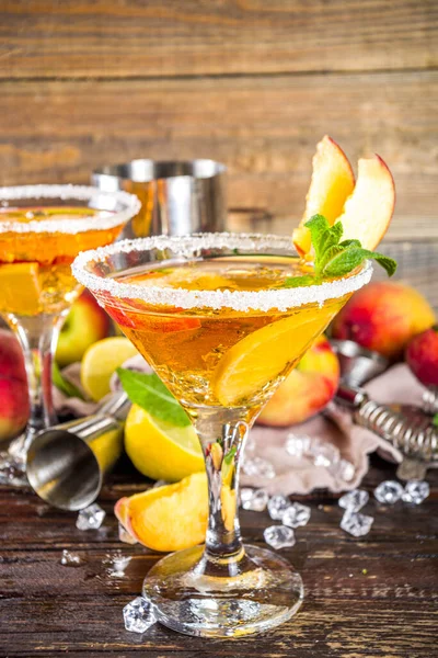 Refreshing summer drink, peach martini cocktails with gin or vodka and fresh peach garnish, wooden background copy space