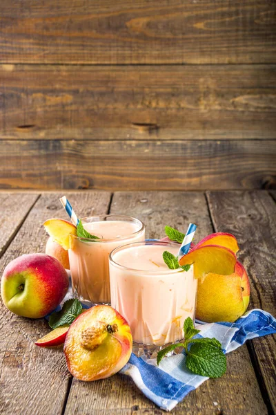 Summer breakfast drink, fresh blended peach smoothie, peach yogurt with nectarine fruit slices, rustic wooden background copy space