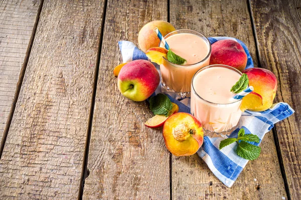 Summer breakfast drink, fresh blended peach smoothie, peach yogurt with nectarine fruit slices, rustic wooden background copy space