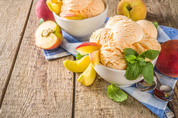 Homemade sweet peach ice cream. Peach gelato balls in small bowls, on wooden background with fresh peaches and mint leaves