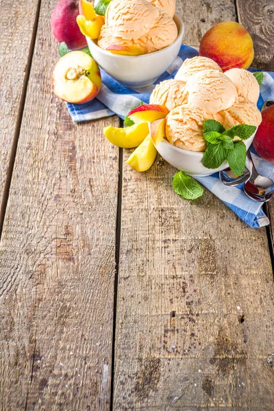 Homemade sweet peach ice cream. Peach gelato balls in small bowls, on wooden background with fresh peaches and mint leaves