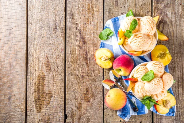 Homemade sweet peach ice cream. Peach gelato balls in small bowls, on wooden background with fresh peaches and mint leaves