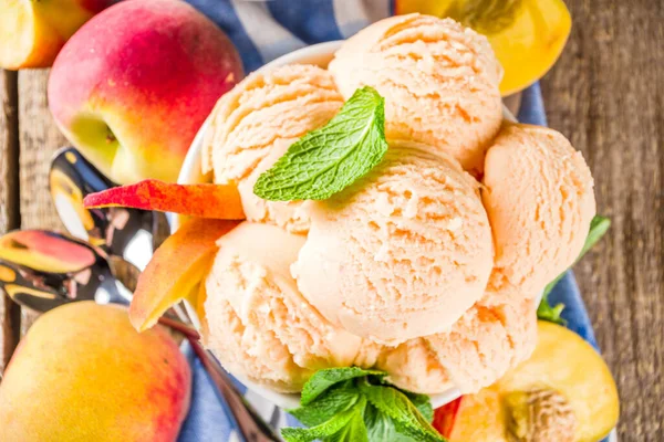 Homemade sweet peach ice cream. Peach gelato balls in small bowls, on wooden background with fresh peaches and mint leaves