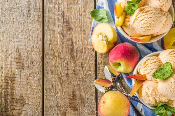 Homemade sweet peach ice cream. Peach gelato balls in small bowls, on wooden background with fresh peaches and mint leaves