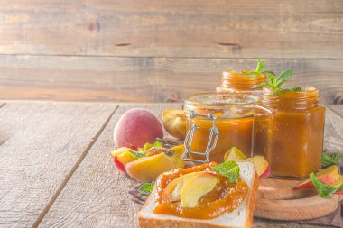 Farklı kavanozlarda ev yapımı şeftali reçeli ve ahşap arka planda taze organik şeftali.