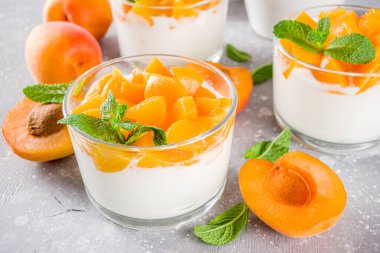 Yaz kahvaltısı tatlısı. Kayısı dilimleri ve naneli yoğurt ve sağlıklı tatlı. Sağlıklı beslenme, vitamin zengini tatlı yiyecekler, gri kayısı arka planında taze kayısılar, kopyalama alanı.