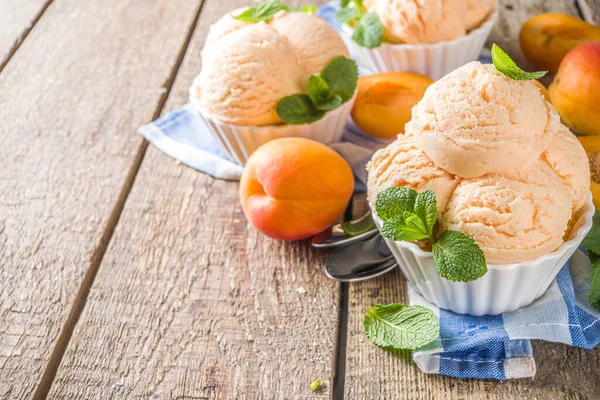 Homemade sweet apricot ice cream. Apricot gelato balls in small bowls, on wooden background with fresh apricots and mint leaves