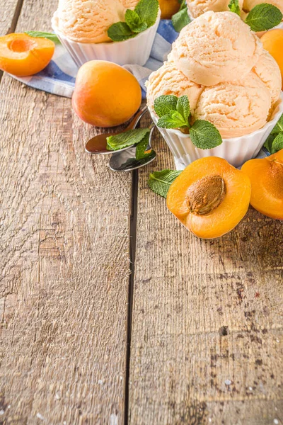 Homemade sweet apricot ice cream. Apricot gelato balls in small bowls, on wooden background with fresh apricots and mint leaves
