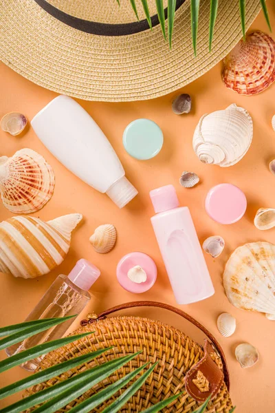 Summer cosmetics background. Summer skincare, sunscreen cosmetics, travel kit miniatures flat lay. Trendy peach background, with women bag, sea shells, tropical leaves, straw hat. Copy space above