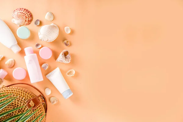 Summer cosmetics background. Summer skincare, sunscreen cosmetics, travel kit miniatures flat lay. Trendy peach background, with women bag, sea shells, tropical leaves, straw hat. Copy space above