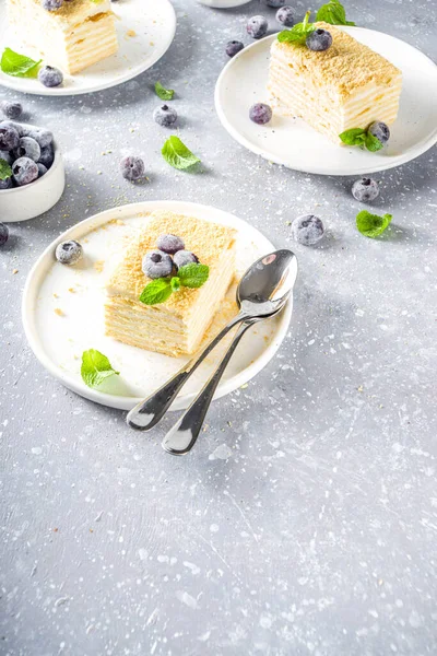 Homemade baked cake Napoleon, Millefeuille. Delicate custard cake garnished with berries and mint. On a gray concrete stone background.