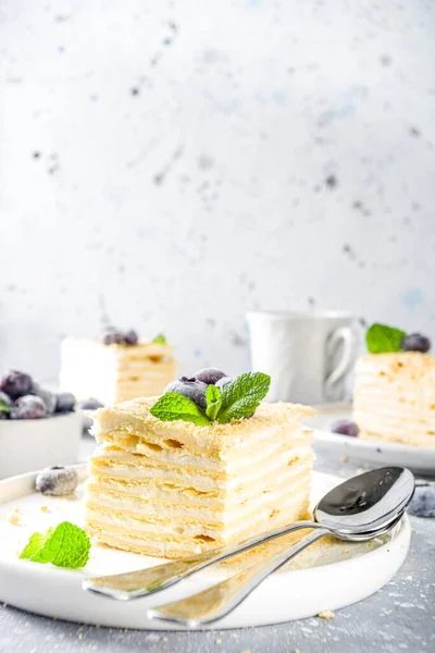Homemade baked cake Napoleon, Millefeuille. Delicate custard cake garnished with berries and mint. On a gray concrete stone background.