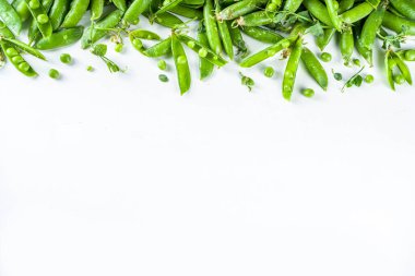 Taze yeşil bezelye kabukları ve beyaz arka planda yeşil bezelyeler, üst manzara. 