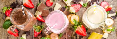 Üç tane milkshake ya da smoothie ile mason kavanozu. Sağlıklı yaz kahvaltısı, öğle yemeği içecekleri - muz, çikolata ve ahşap arka planda çilekli milkshake.