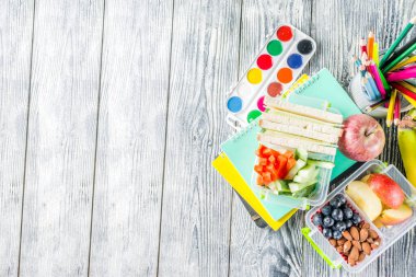 Sağlıklı bir okul yemeği kutusu. Sandviç, meyve, sebze, fındık, su ve okul malzemeleri ile çocuk öğle yemeği kutusu, Beyaz ahşap arka plan