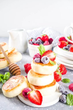 Bal sürülmüş süzme peynir krepleri ve gri arka planda çeşitli yaz meyveleri, yaz kahvaltısı veya öğle yemeği