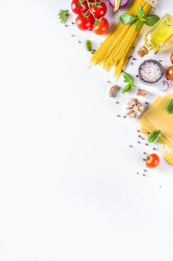 Makarna pişirmek için İtalyan yemekleri. Çeşitli malzemeli çiğ spagetti makarna - soğan, domates, sarımsak, fesleğen, maydanoz, peynir, zeytinyağı. Beyaz tablo arkaplanında, düz kopya alanı