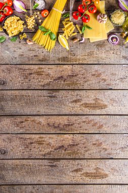 Çeşitli çiğ makarna ve baharatlar. Taze otlar ve sebzelerle İtalyan makarnası pişirmek. Rustik biçim, ahşap arkaplan üst görünüm kopyalama alanı