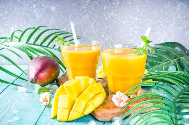 Taze tropikal meyve suyu. Mango smoothie veya mango suyu, taze mango ve açık hava ahşap arka planında tropikal yapraklar. Üst görünümü kopyala.