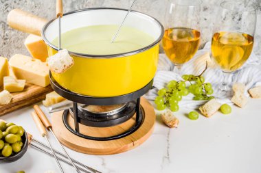 Çatallar, çeşitli peynirler, zeytin, ekmek ve üzüm, beyaz mermer arka plan kopya alanı ile geleneksel fondü tencerede gurme İsviçre fondü