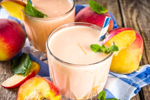 Summer breakfast drink, fresh blended peach smoothie, peach yogurt with nectarine fruit slices, rustic wooden background copy space