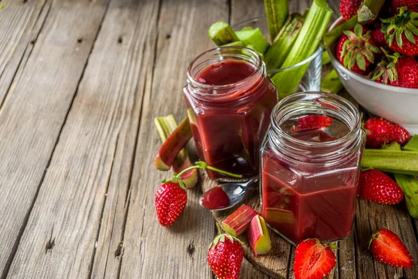 Homemade strawberry rhubarb jam or sauce, with fresh rhubarb and strawberries and spices, wooden rustic background copy space