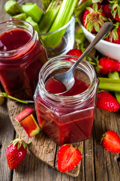 Homemade strawberry rhubarb jam or sauce, with fresh rhubarb and strawberries and spices, wooden rustic background copy space