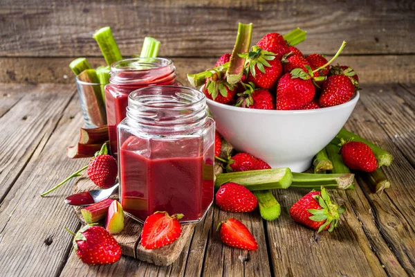 Homemade strawberry rhubarb jam or sauce, with fresh rhubarb and strawberries and spices, wooden rustic background copy space