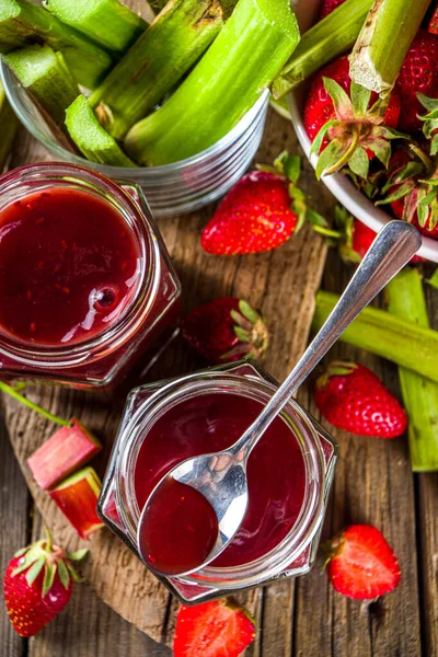 Homemade strawberry rhubarb jam or sauce, with fresh rhubarb and strawberries and spices, wooden rustic background copy space