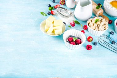 Böğürtlenli kek tarifi. Yaz pişirme arka planında çeşitli böğürtlenler, pişirme malzemeleri, aletler ve çatallar, açık mavi güneş ahşap arka planda düz bir zemin oluşturur.