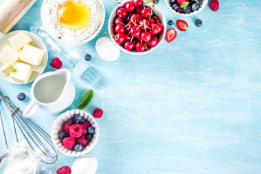 Böğürtlenli kek tarifi. Yaz pişirme arka planında çeşitli böğürtlenler, pişirme malzemeleri, aletler ve çatallar, açık mavi güneş ahşap arka planda düz bir zemin oluşturur.