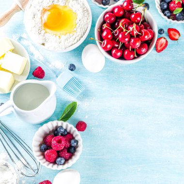 Böğürtlenli kek tarifi. Yaz pişirme arka planında çeşitli böğürtlenler, pişirme malzemeleri, aletler ve çatallar, açık mavi güneş ahşap arka planda düz bir zemin oluşturur.