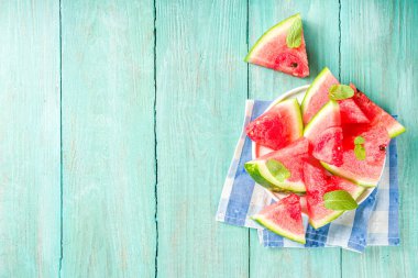 Yaz tatili konsepti. Denizde yaz tatili. Kadın mayosu, şort ve hasır şapka. Mavi ahşap arka planda karpuz dilimleri ve deniz kabukları var. Üst görünüm kopyalama alanı oluştur