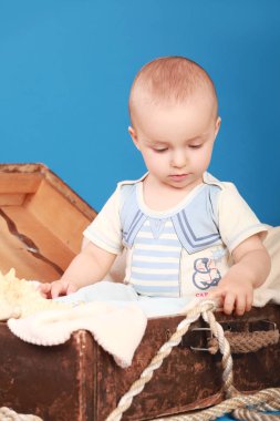 Bir çocuk bir göğüs denizci elbiseli oturur ve ip görünüyor