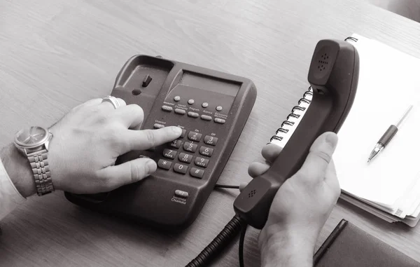 İşadamı sabit hat telefon numarasını çevirir, yakışıklı sağ elinde tutar. Yakınlarda bir defter ve kalem var. Çerçevede el tek eller, saat ve yüzük. Siyah ve beyaz fotoğraf