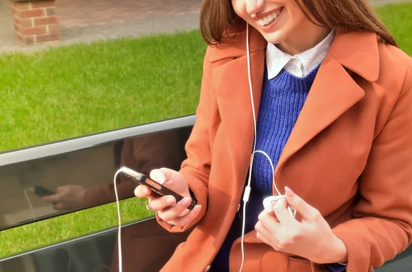 The woman is sitting, holds the phone in her hands and listens to music