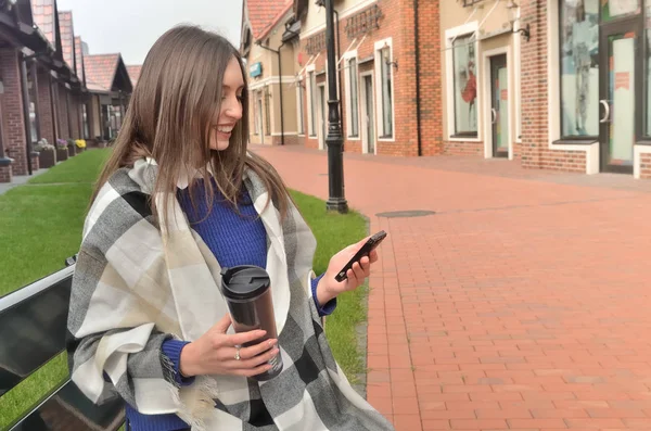 Sonriente mujer está sentada en un banco, envuelta en un cuadros —  Fotos de Stock