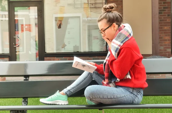Asian girl sits on a bench and reads a book