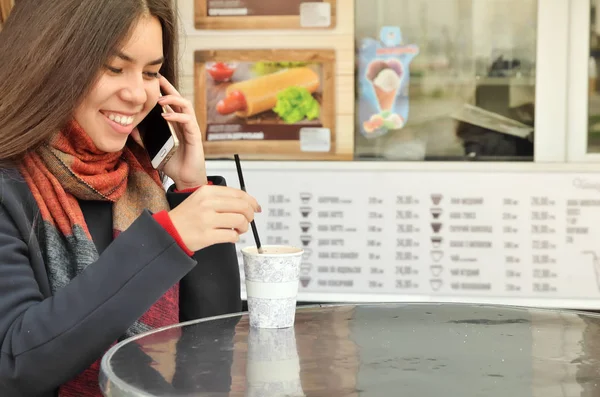 Asian woman puts coffee and speaks by telephone.