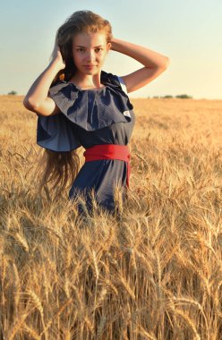 Güzel bir genç kadın uzun saçlı ayakta buğday alanı ile. Saçlarını dokunur