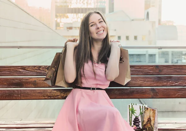 Chica feliz sentada en el banco, sosteniendo compras en sus manos —  Fotos de Stock