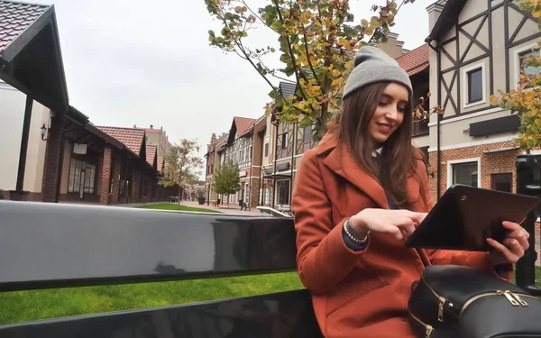 Hermosa joven sentada en un banco y disfrutando de una tableta —  Fotos de Stock