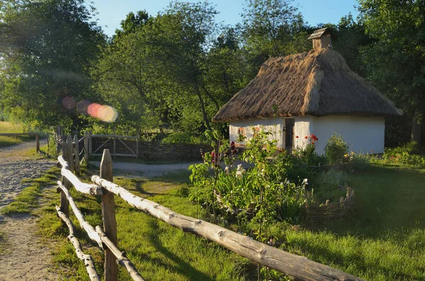 Una pequeña cabaña ucraniana con un techo de paja rodeado por una valla de madera —  Fotos de Stock