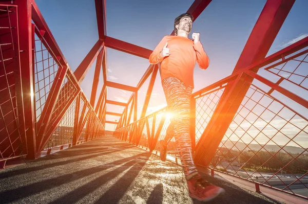 Jovem correndo na ponte de metal ao pôr do sol — Fotografia de Stock