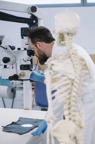 Scientifique en laboratoire qui regarde le microscope et un squelette — Photo