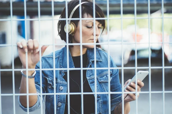 Gadis berambut cokelat dengan headphone dan smartphone di jalan — Stok Foto