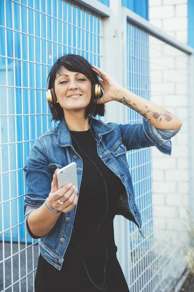 Gadis berambut cokelat dengan headphone dan smartphone di jalan — Stok Foto