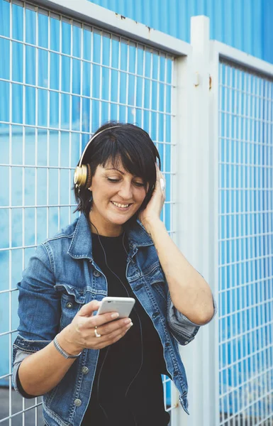 Gadis berambut cokelat dengan headphone dan smartphone di jalan — Stok Foto